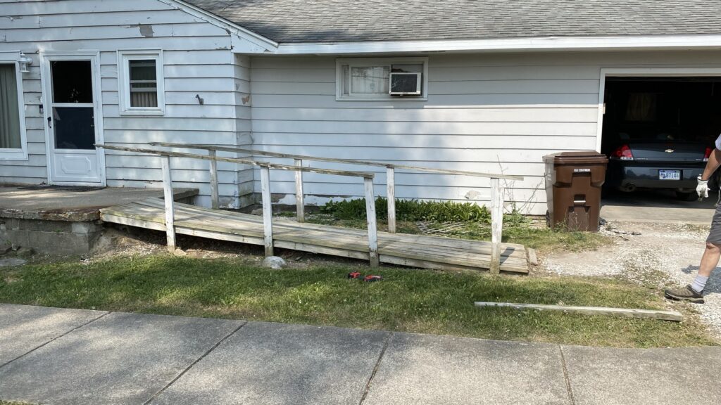 Old wooden wheelchair ramp in poor condition leading to front door, showing unsafe and unstable construction